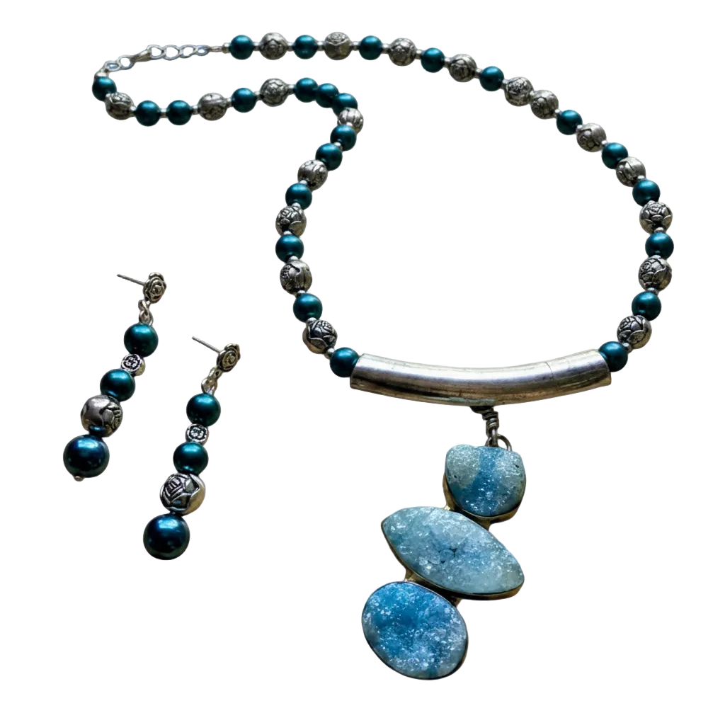 A jewelry set featuring a silver-toned beaded necklace with a curved bar and three stacked blue agate pendants, accompanied by matching drop earrings with dark teal and silver beads, shown on a plain white background.