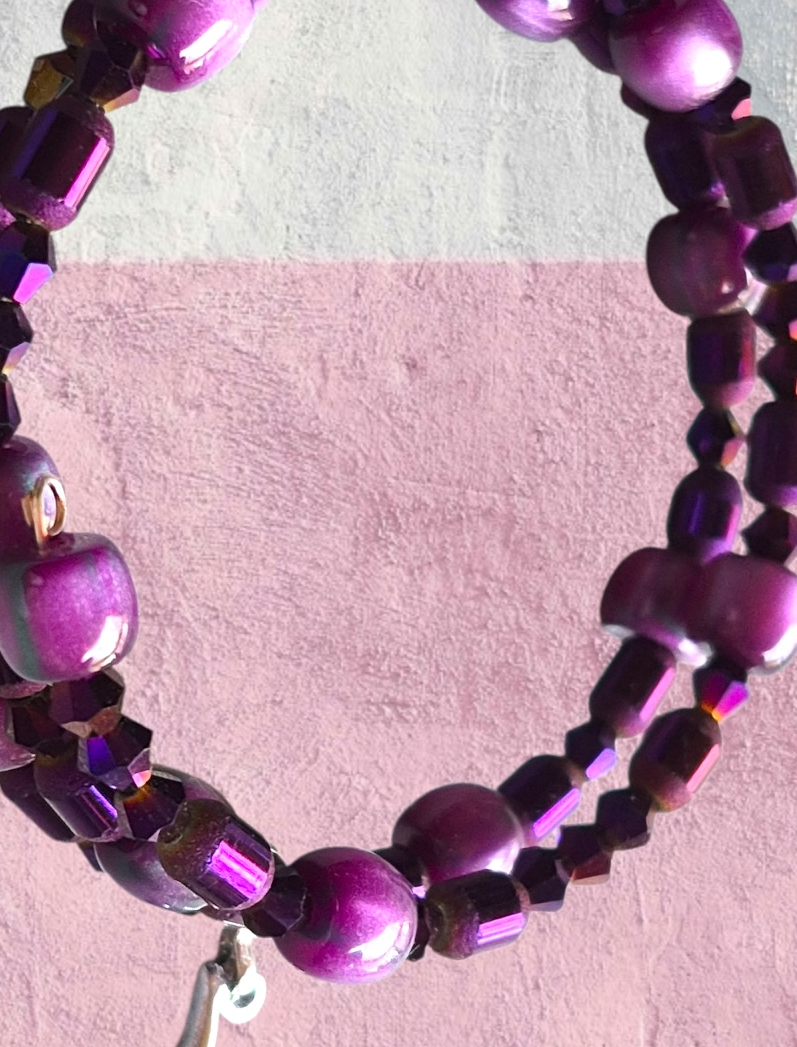 A display of pair of purple beaded drop earrings and a matching purple beaded  wrap bracelet.  A focal bead in each earring and throughout the bracelet add interest to the set as they catch and reflect light!