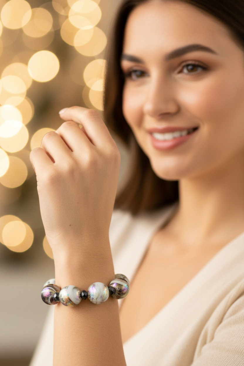 A woman wearing a beaded bracelet with white, black, and iridescent beads, posing in front of warm, blurred holiday lights.