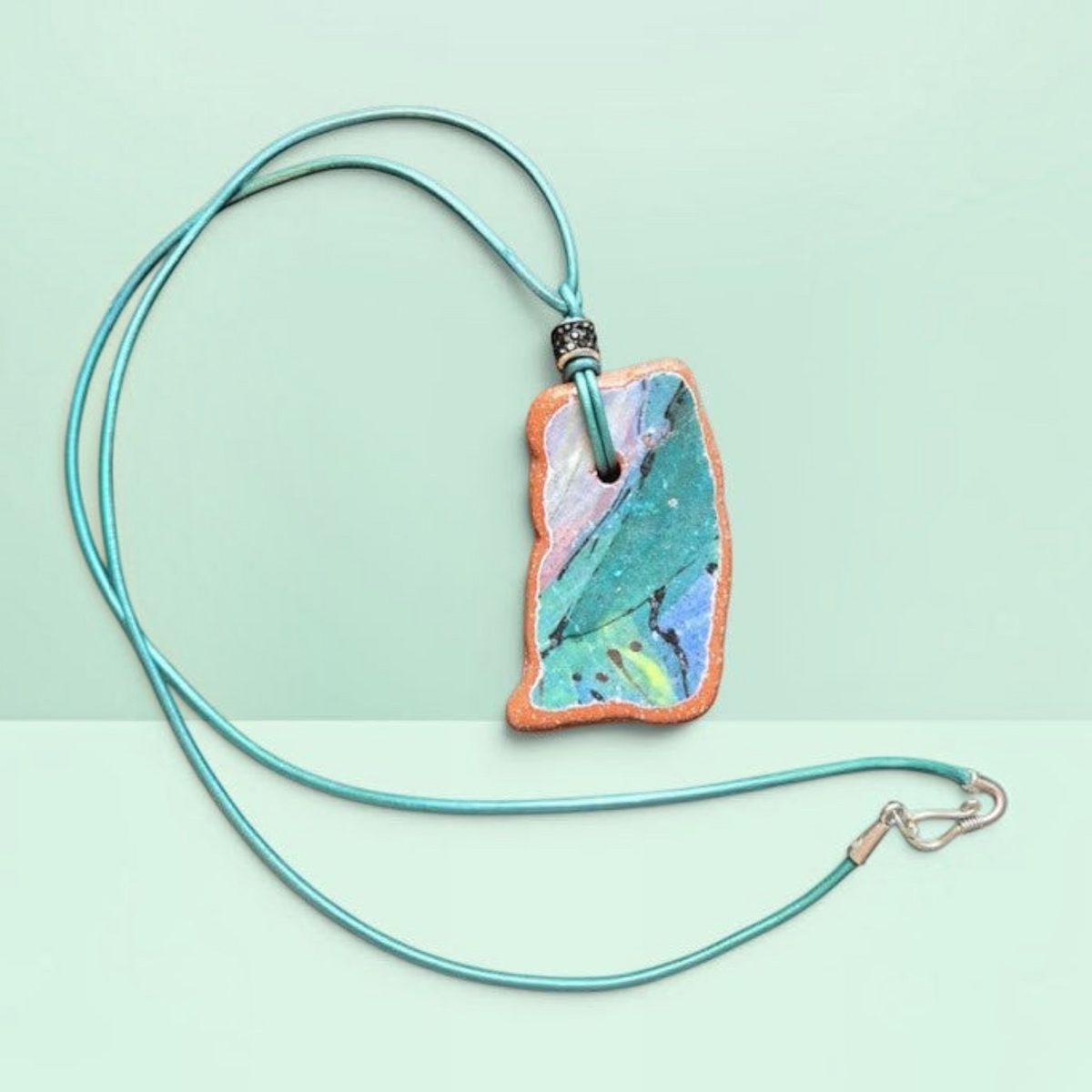 Heartfelt Creations artisan ceramic pendant necklace with teal, blue, and pink crackled glaze on a teal leather cord.