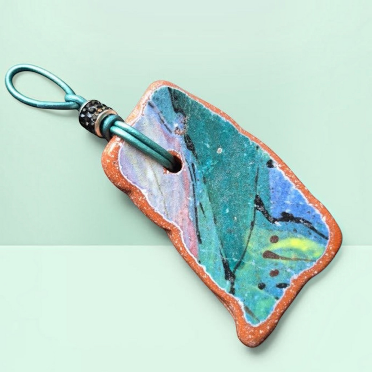 Heartfelt Creations artisan ceramic pendant necklace with crackled teal, blue, and pink glaze on a teal leather cord.