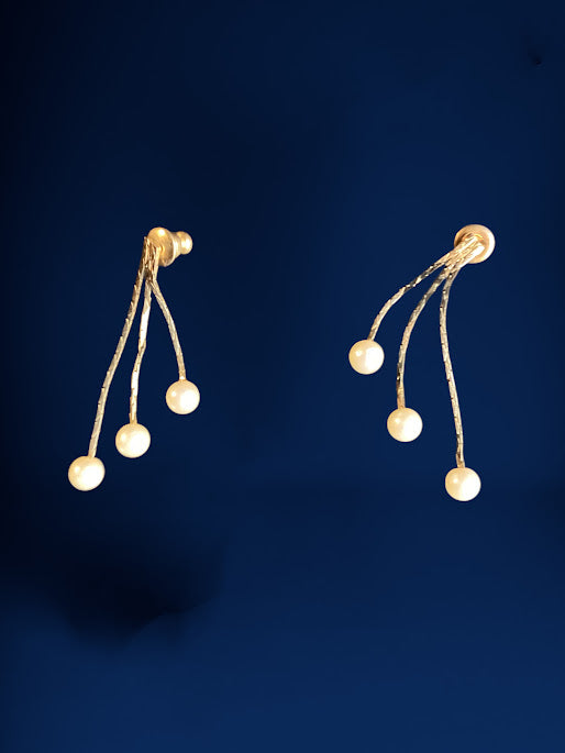 A pair of gold dangle earrings with six small white pearl beads on each earring, set against a dark navy blue background.