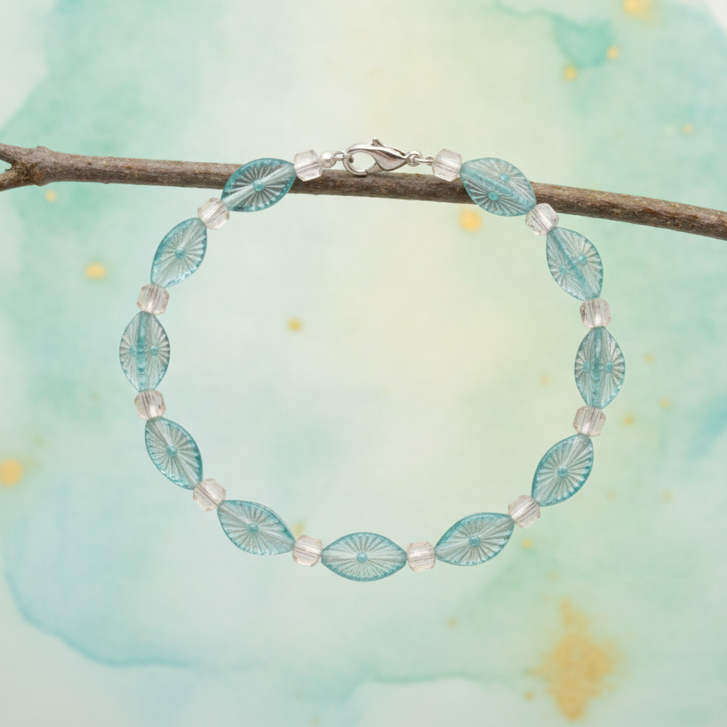 a delicate bracelet featuring alternating oval-shaped, light blue glass beads with a textured sunburst pattern and smaller, clear, faceted glass beads, secured with a silver-toned clasp.