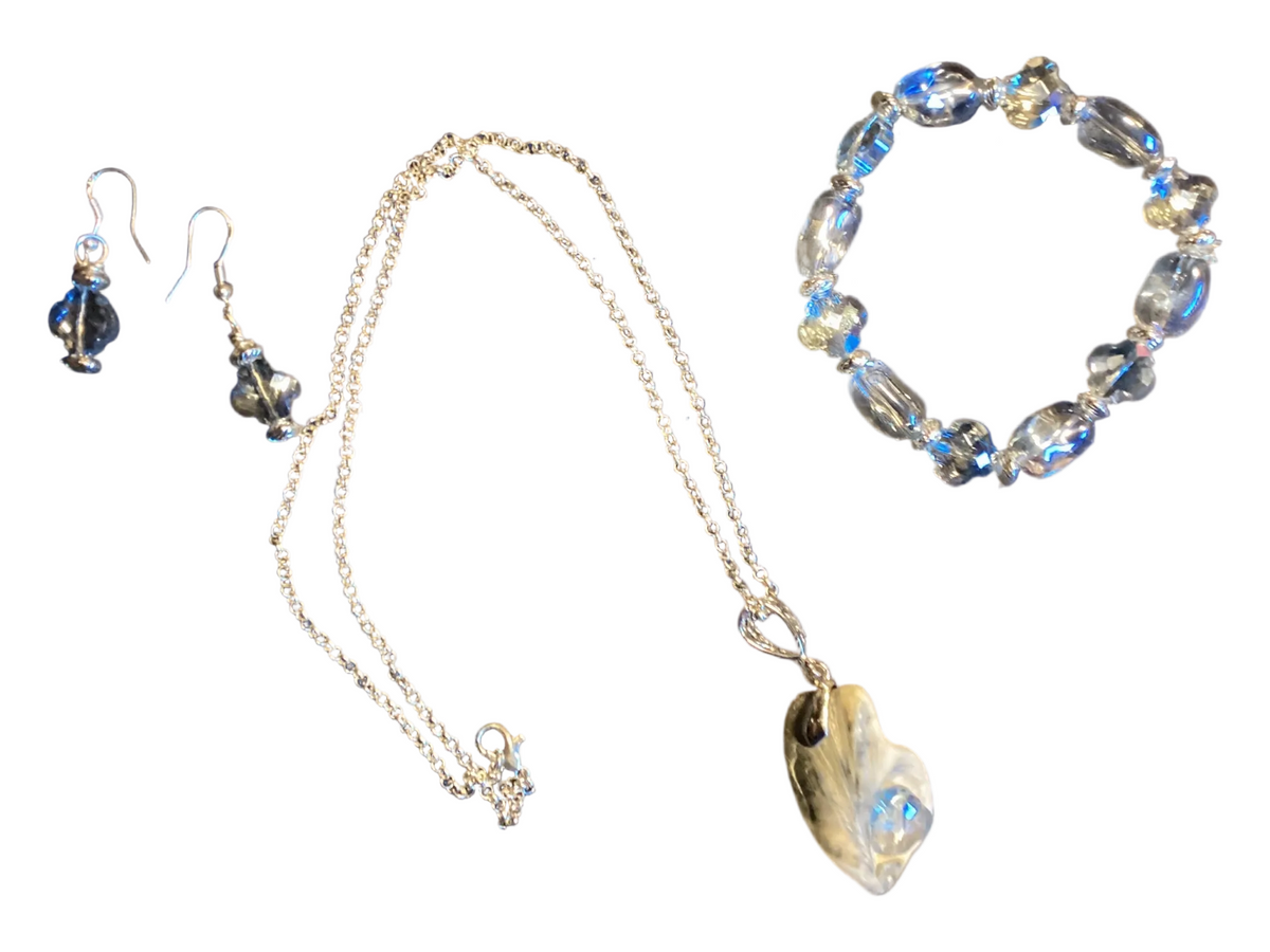 A jewelry set featuring a silver-tone chain necklace with a large iridescent shell pendant, matching drop earrings, and a beaded bracelet with blue and clear faceted beads, displayed on a solid white background.