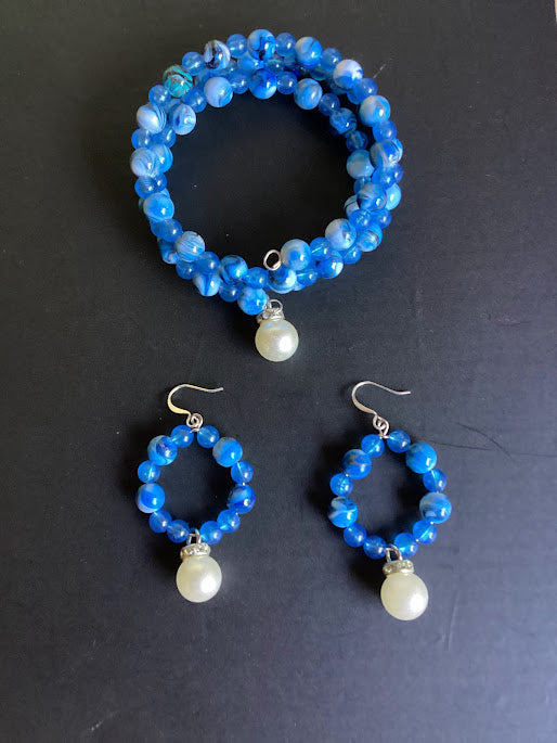 Blue beaded bracelet and earrings with pearl drops on a black background