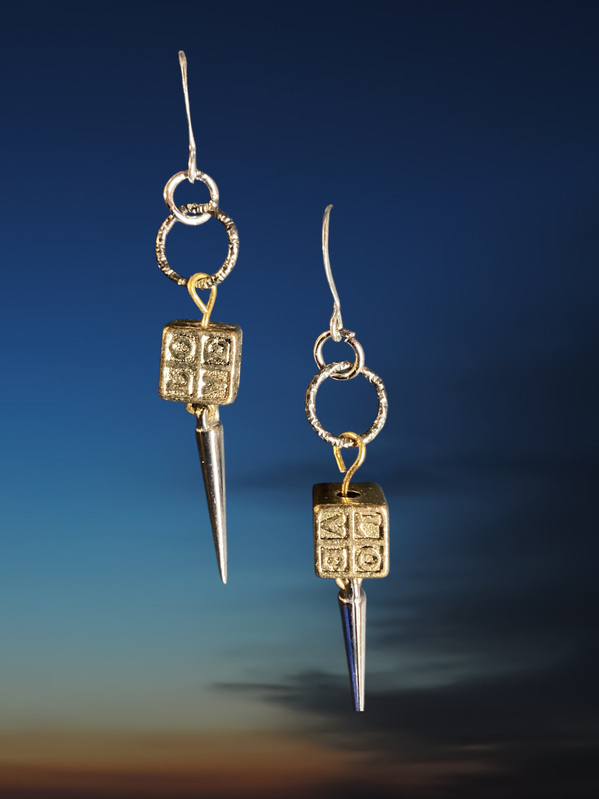Pair of earrings with gold and silver designs on a blue gradient background