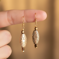 Pair of gold earrings with intricate designs on a soft focus background