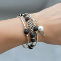 Stack of silver and black beaded bracelets on a purple textured background