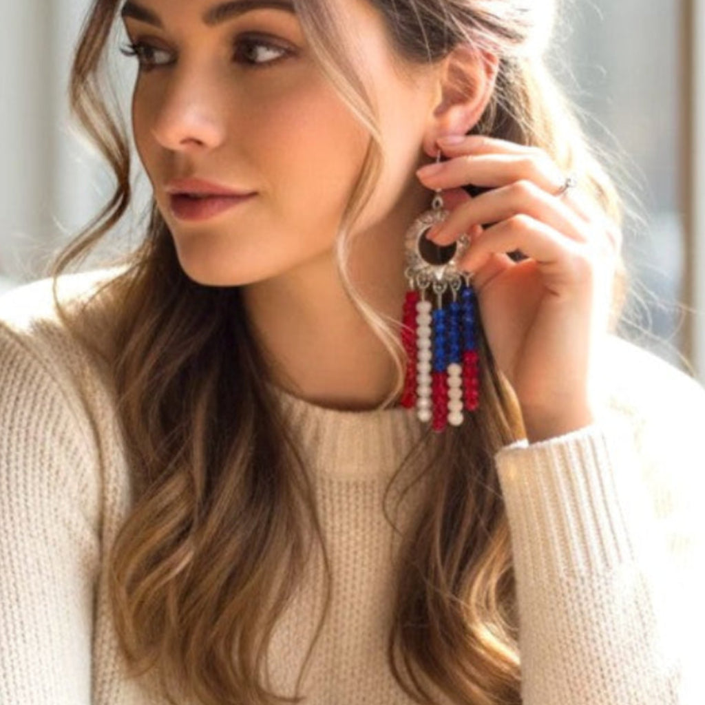 Heartfelt Creations patriotic beaded fringe dangle earrings in red, white, and blue worn by a woman in a cafe.