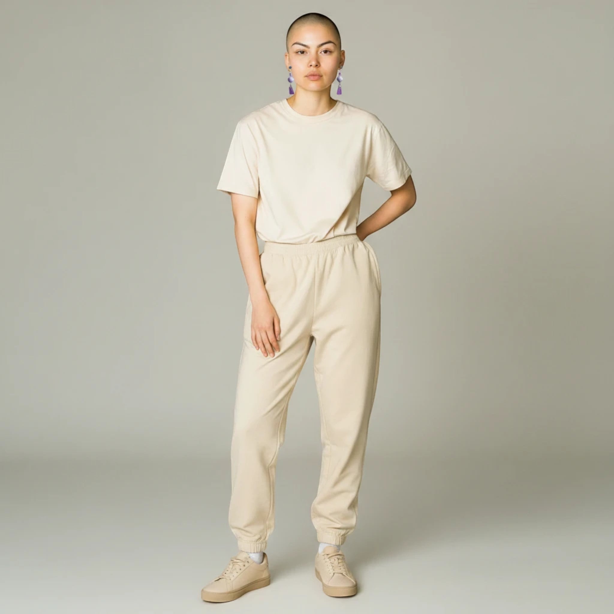 Model wearing Heartfelt Creations floral amethyst dangle earrings with a beige loungewear set against a grey background