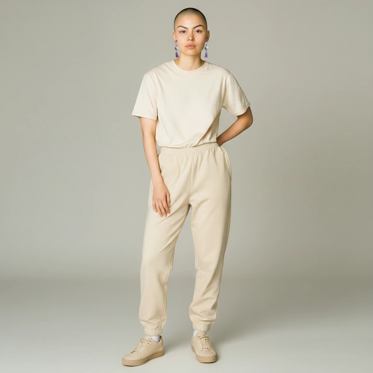 Model wearing Heartfelt Creations floral amethyst dangle earrings with a beige loungewear set against a grey background