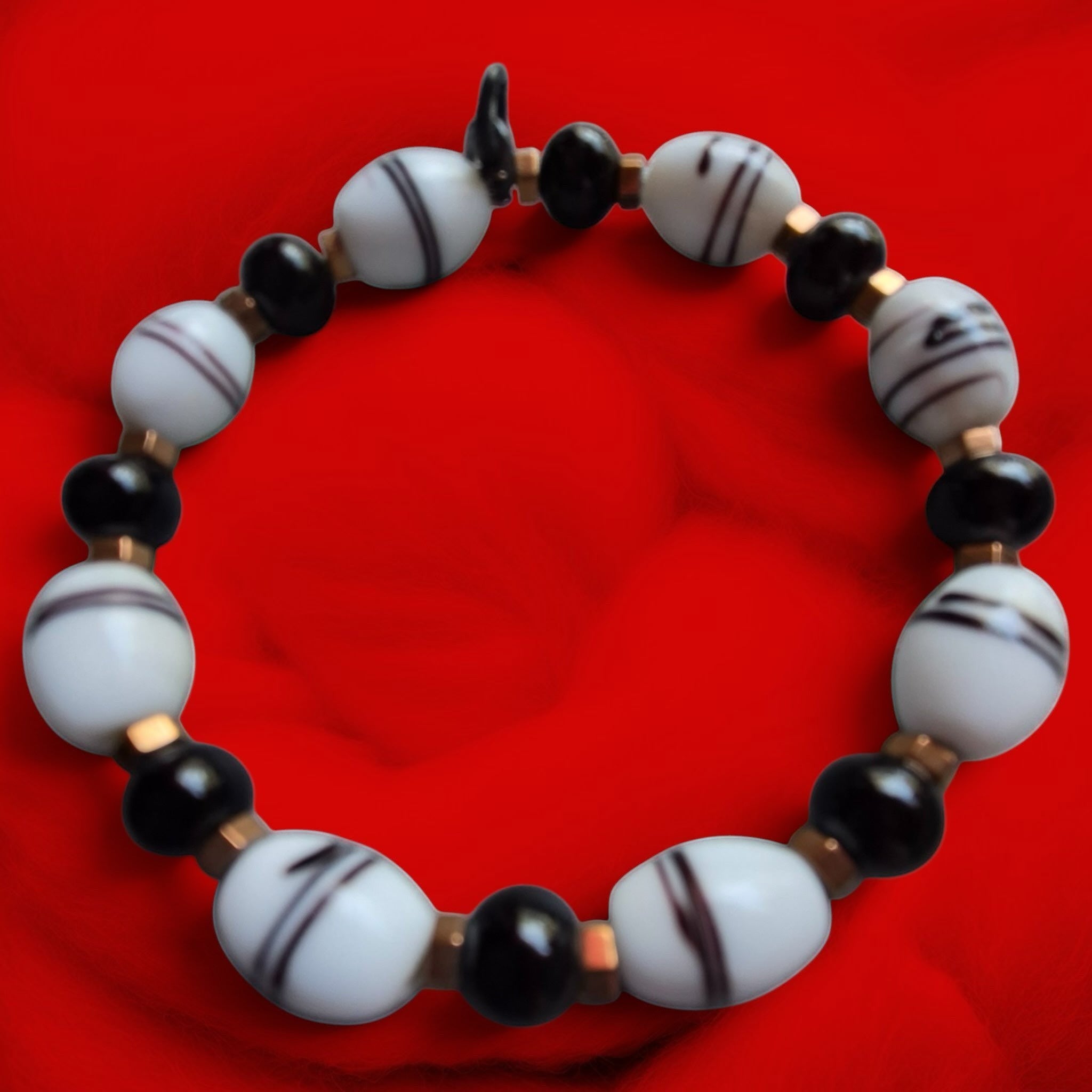 Heartfelt Creations beaded bracelet with black beads, striped white oval beads, and a silver dolphin charm on red fabric