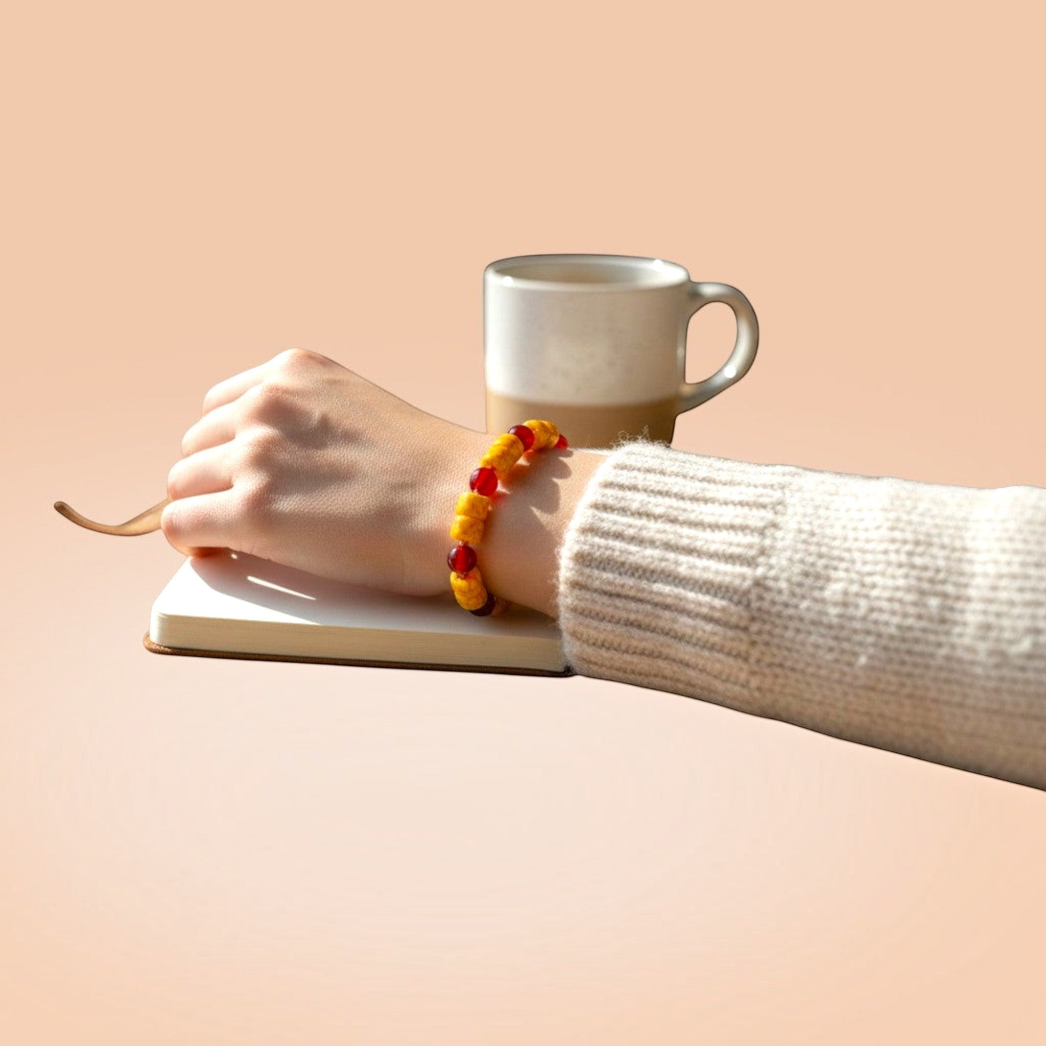 Heartfelt Creations beaded bracelet with yellow crackle and red beads worn on a wrist next to a notebook and mug