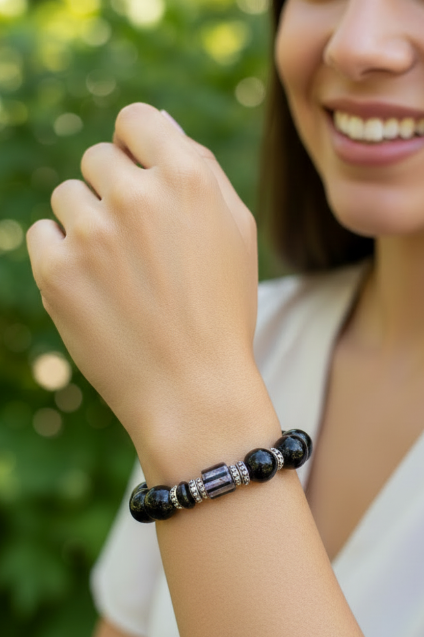A woman outdoors wearing a beaded bracelet with dark blue and black beads, silver spacer beads, and a central metallic cylindrical accent.