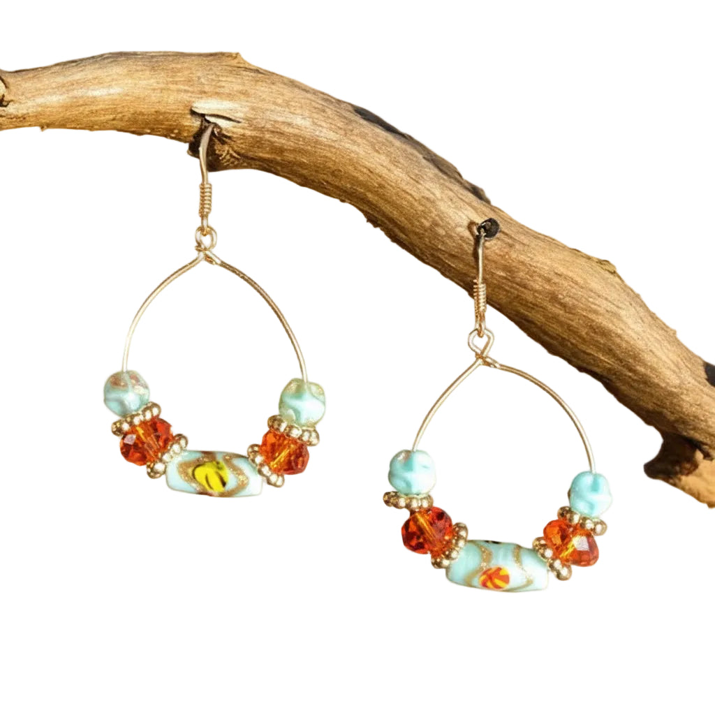 Heartfelt Creations artisan teardrop hoop earrings featuring turquoise and amber glass beads on a rustic branch