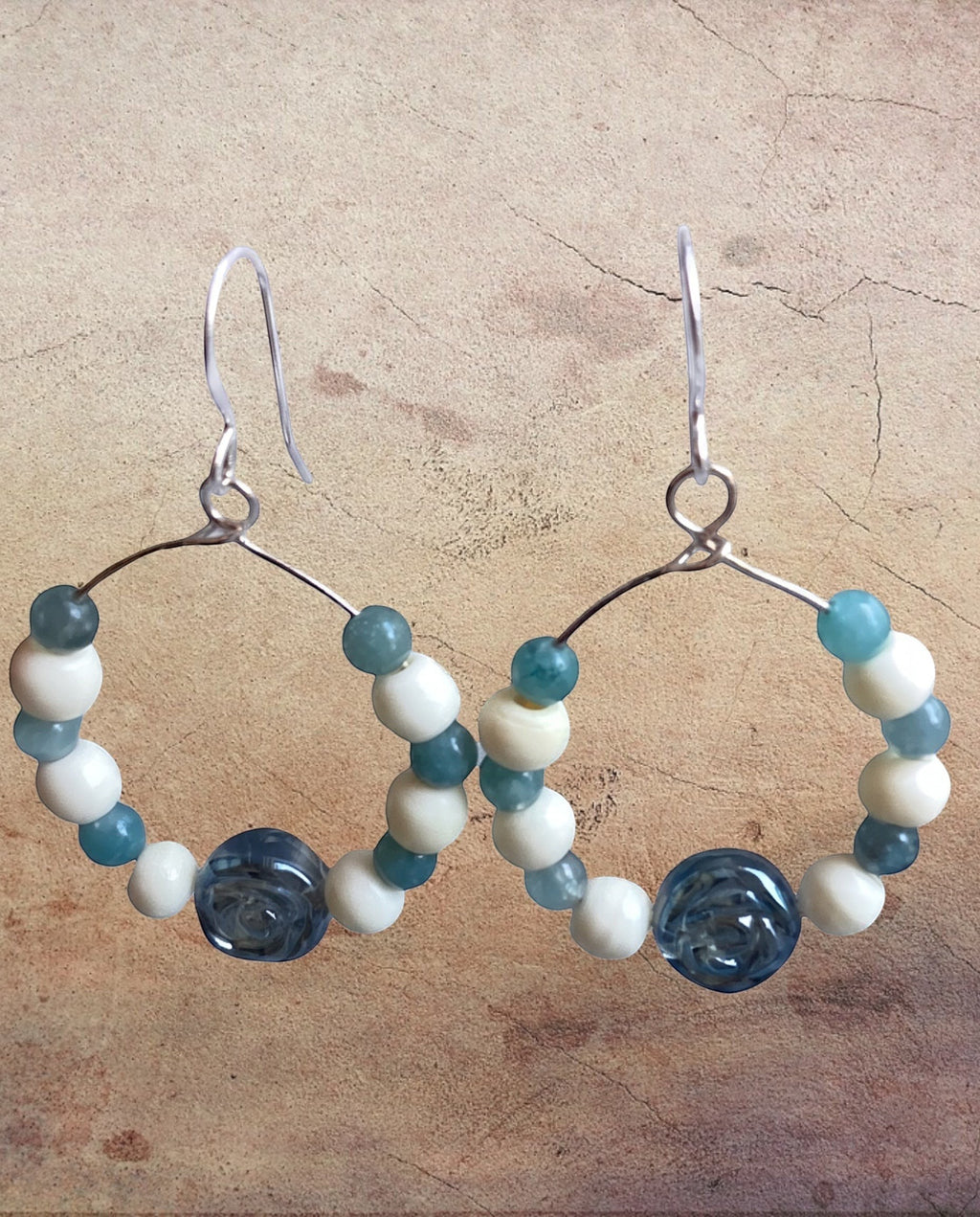 Heartfelt Creations artisan hoop earrings featuring blue and off-white beads with floral-carved glass accents