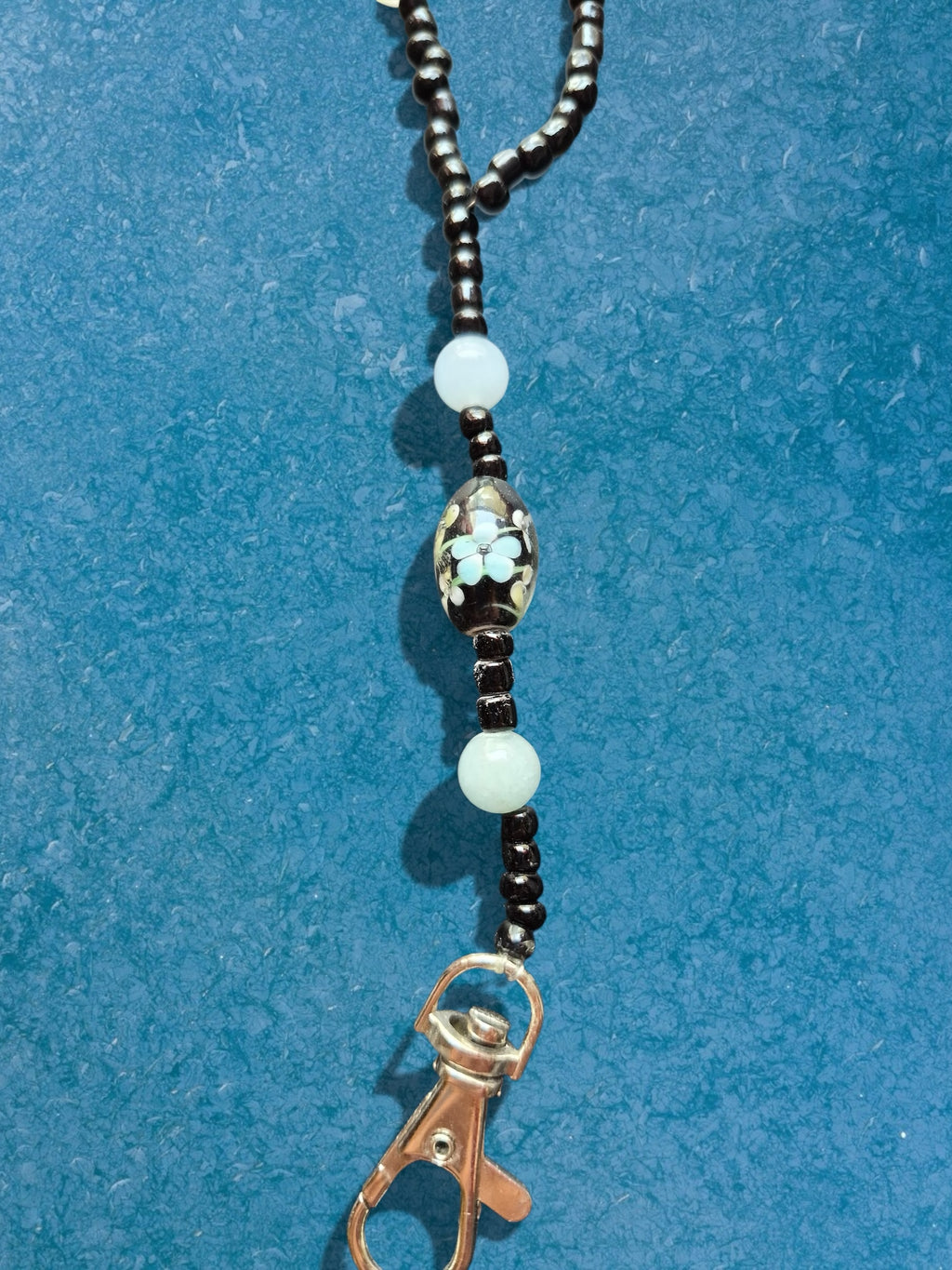 Heartfelt Creations beaded lanyard with black seed beads, light blue accents, floral bead, and silver-tone clasp.