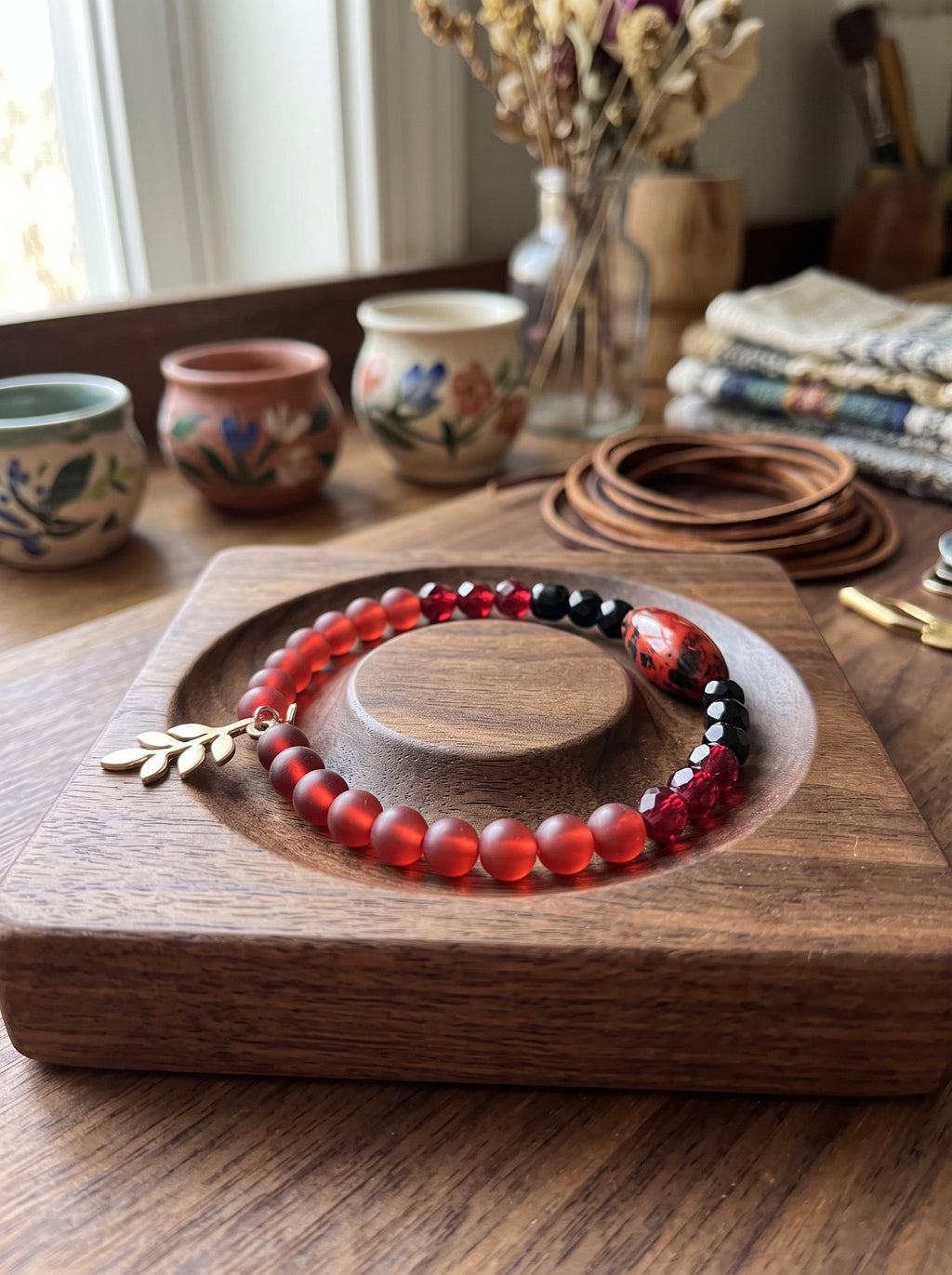 Heartfelt Creations beaded wire wrap bracelet with crimson matte beads, black accents, and a gold-toned leaf charm.