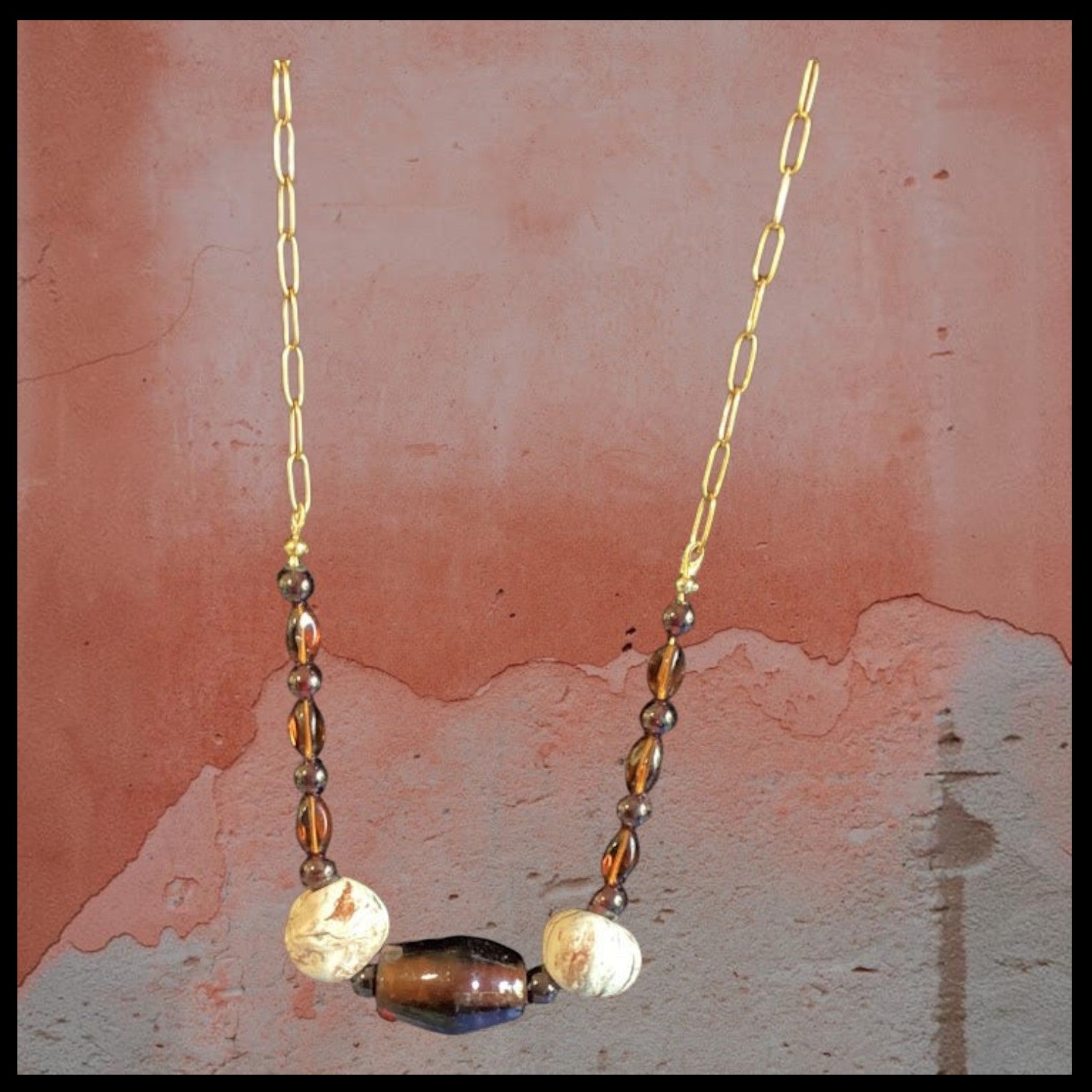 Heartfelt Creations bohemian statement necklace with a gold chain, translucent brown bead, and cream-colored stones.