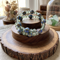Heartfelt Creations artisan wrap bracelet with green glass and hand-painted blue ceramic beads on a wooden display.