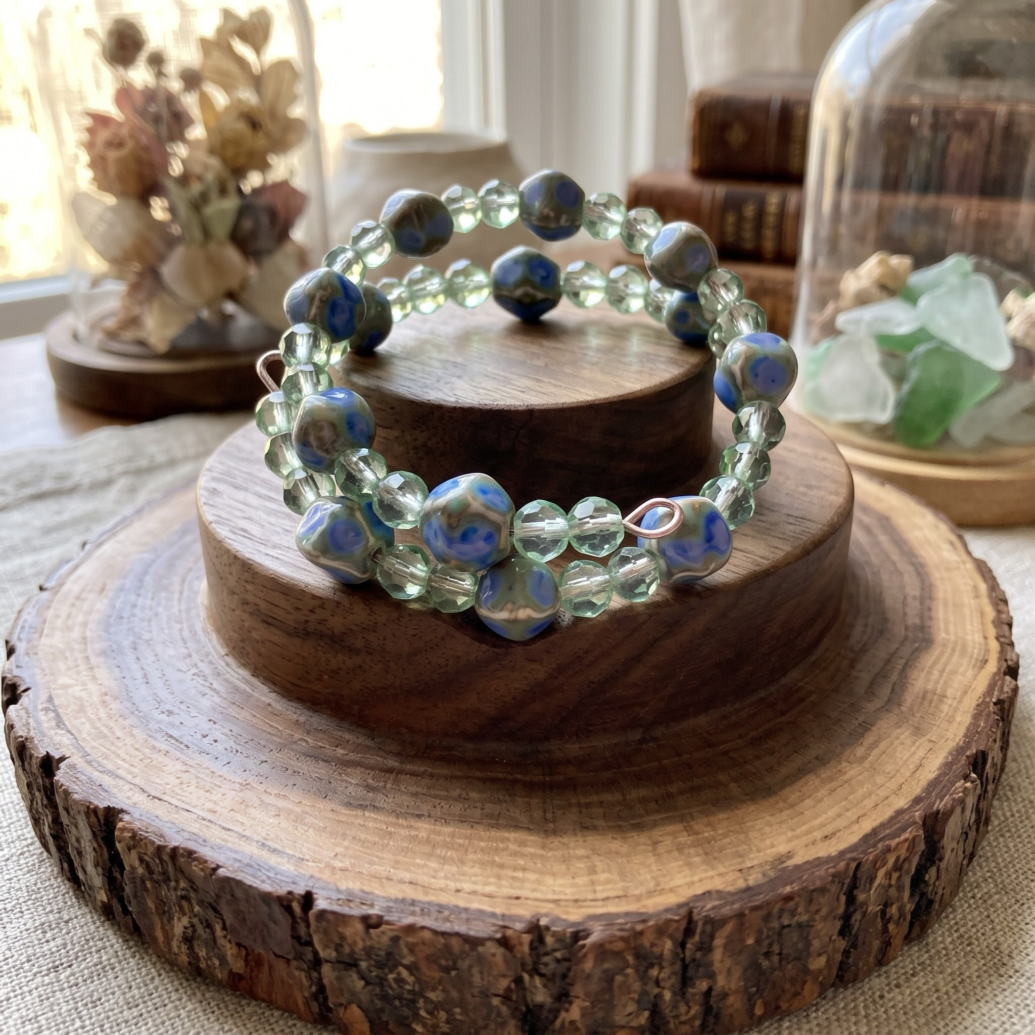 Heartfelt Creations artisan wrap bracelet with green glass and hand-painted blue ceramic beads on a wooden display.