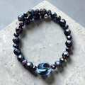 Heartfelt Creations black faceted beaded wrap bracelet with a central iridescent circular charm on concrete surface.