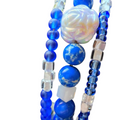 Close-up of a beaded jewelry strand featuring royal blue glass beads, marbled blue and white beads, a large iridescent white flower-shaped bead, and clear faceted beads on a white background.