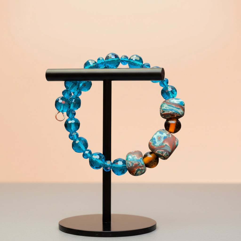 A beaded stretch bracelet displayed on a black T-stand. The bracelet features translucent bright blue faceted beads, a large marbled blue and brown bead, and two dark brown tiger-eye style beads.