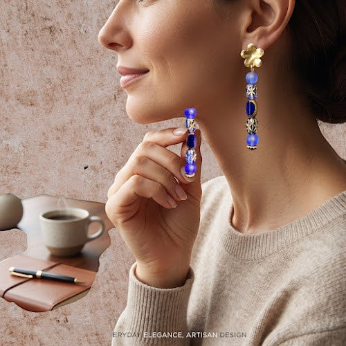 Heartfelt Creations artisan blue beaded drop earrings with gold floral accents worn by a woman in a cozy setting