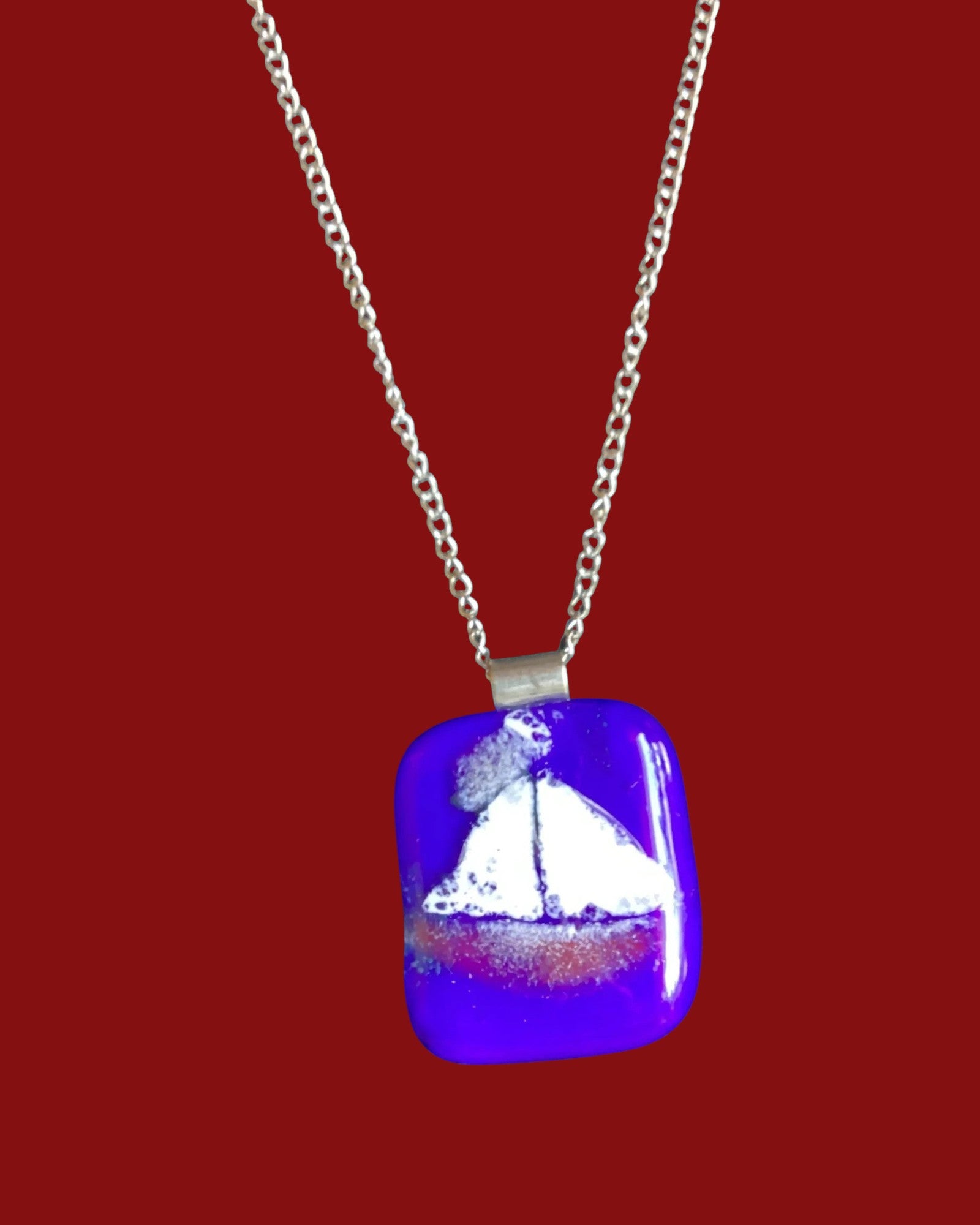 Heartfelt Creations fused glass pendant necklace featuring a minimalist white sailboat on a deep blue background. 