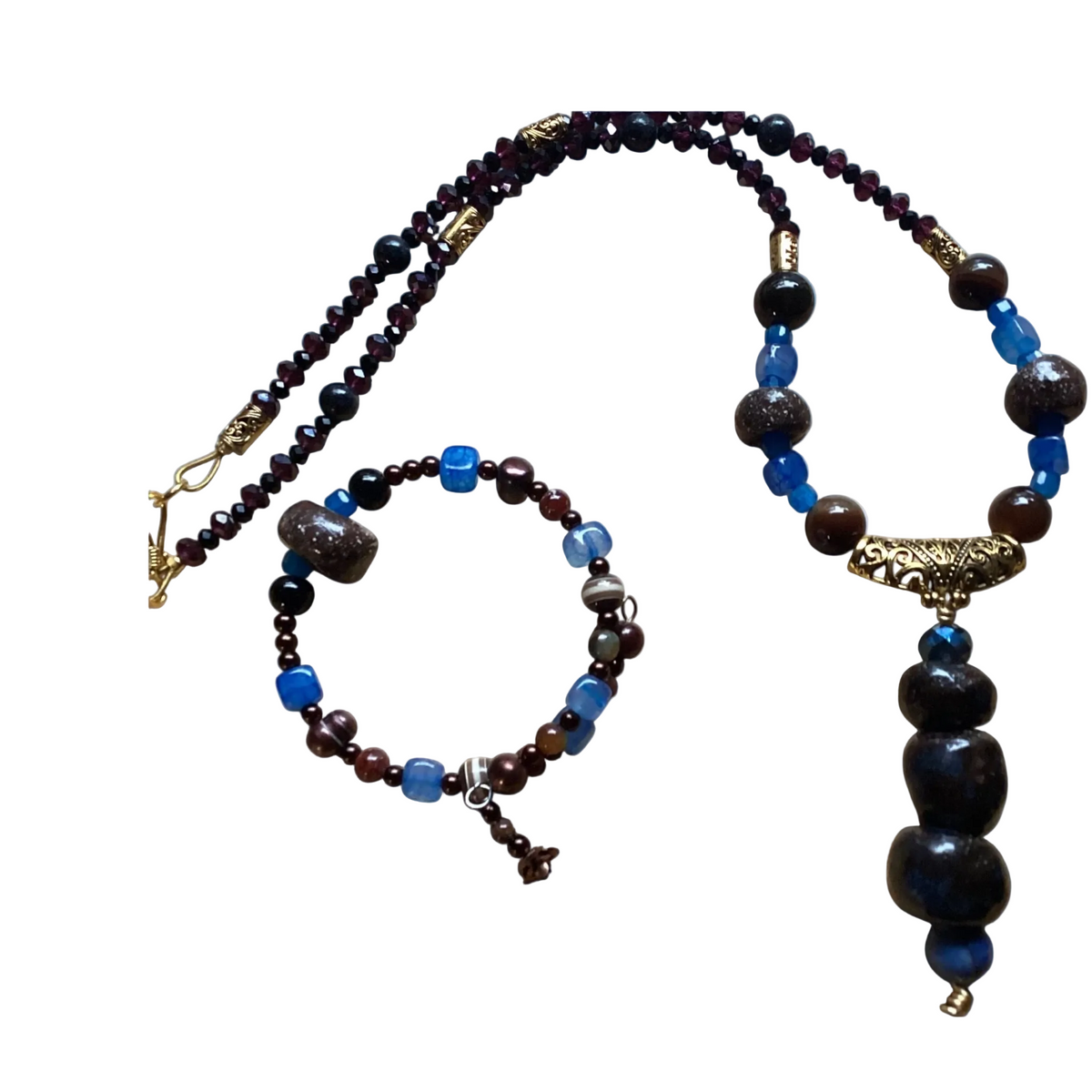 A beaded necklace and matching bracelet set on a plain white background. The jewelry features dark brown and black polished beads, bright blue translucent beads, and antique gold-toned metal accents, including a decorative clasp and a tassel.