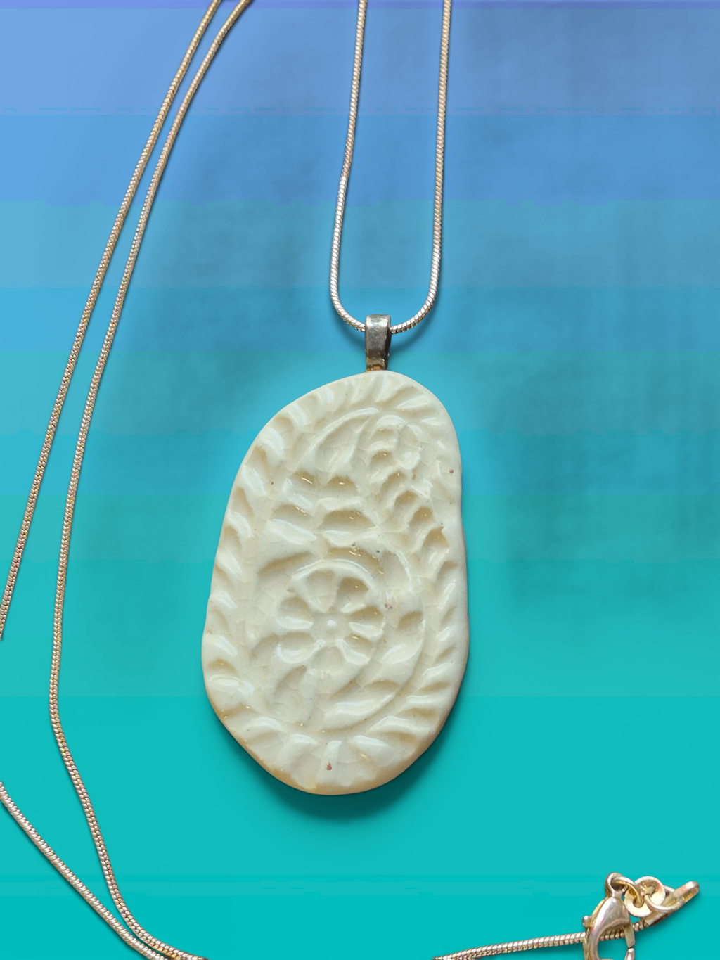 Heartfelt Creations off-white ceramic pendant necklace with embossed floral motif and crackle glaze on metallic chain.