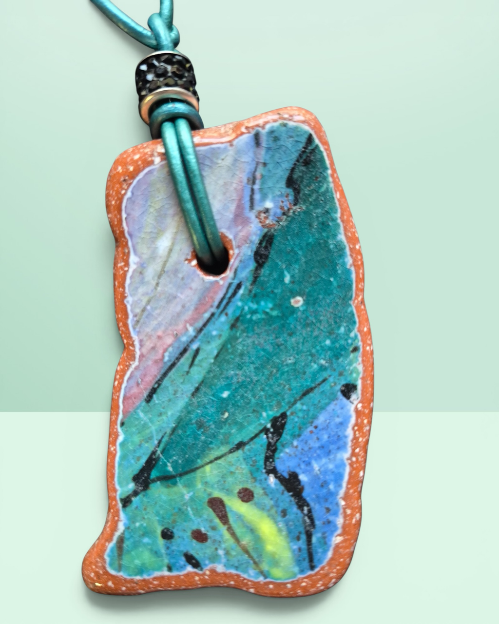 Heartfelt Creations artisan ceramic pendant necklace with crackled teal, blue, and pink glaze on a teal leather cord.