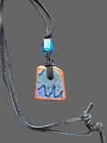 Heartfelt Creations artisan ceramic pendant necklace with blue teal and orange crackle glaze on a black suede cord.