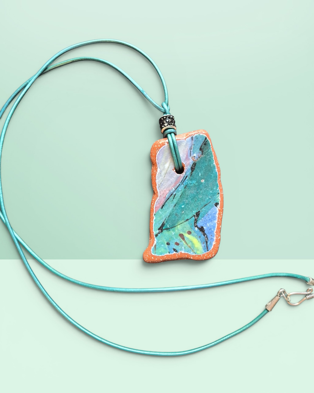 Heartfelt Creations artisan ceramic pendant necklace with crackled teal, blue, and pink glaze on a teal leather cord.