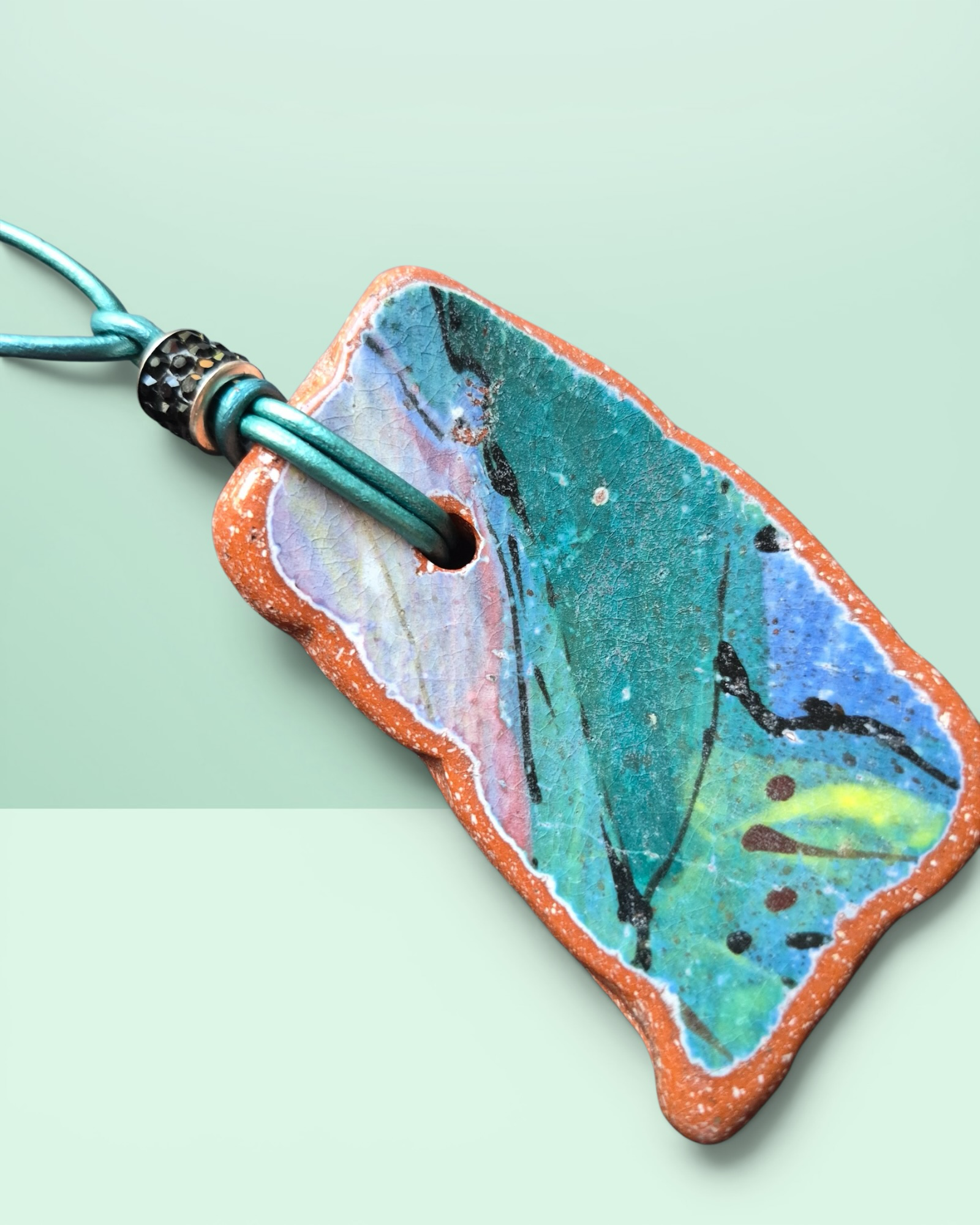 Heartfelt Creations artisan ceramic pendant necklace with crackled teal, blue, and pink glaze on a teal leather cord.