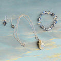 Heartfelt Creations silver-tone jewelry set with blue-grey crystal beads, iridescent pendant necklace, drop earrings, and bracelet.