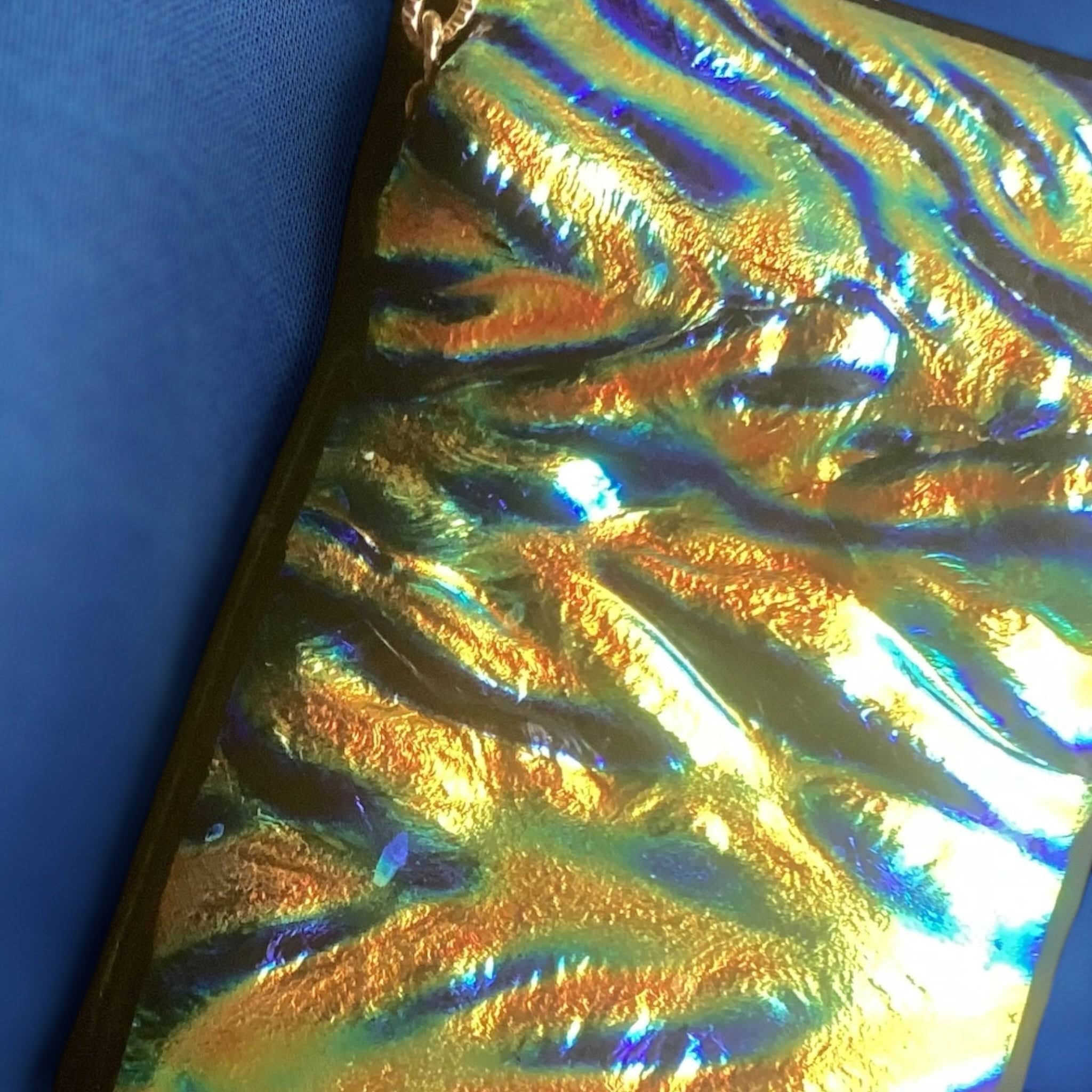 rectangular, iridescent dichroic glass pendant with a wavy, textured surface in shimmering shades of gold, green, and blue, suspended from a delicate, thin gold-colored chain with a small clasp