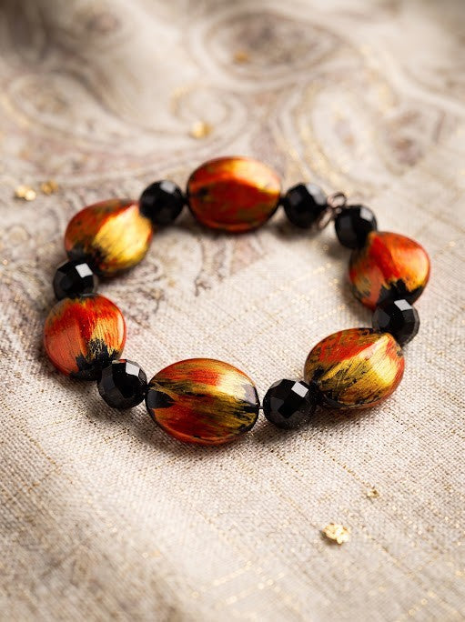 Heartfelt Creations artisan bracelet with oval fire-colored beads and black faceted accents on a textured fabric