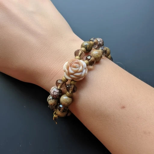 Beaded bracelet with a rose charm on a wrist against a dark background