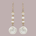 A pair of gold and white drop earrings featuring baroque pearls, faceted beads, and ornate gold metalwork, displayed against a solid muted mauve background.