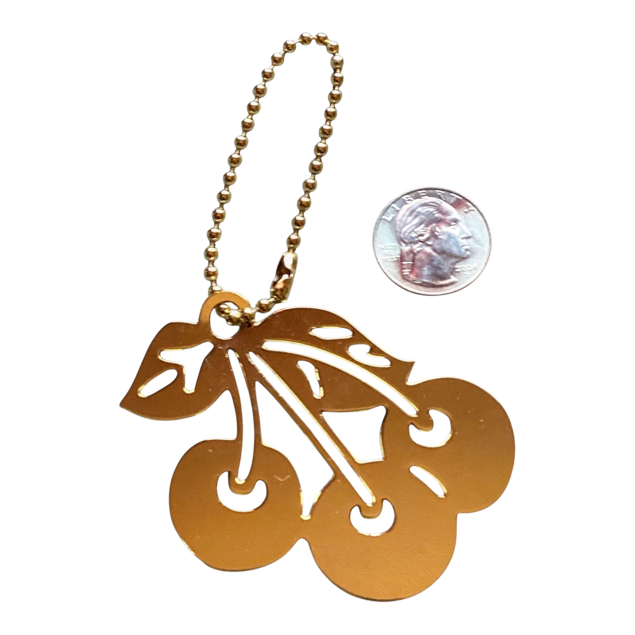 A gold-colored metal cherry keychain with a ball chain and a cherry cutout pendant, shown next to a US quarter for scale on a white background.