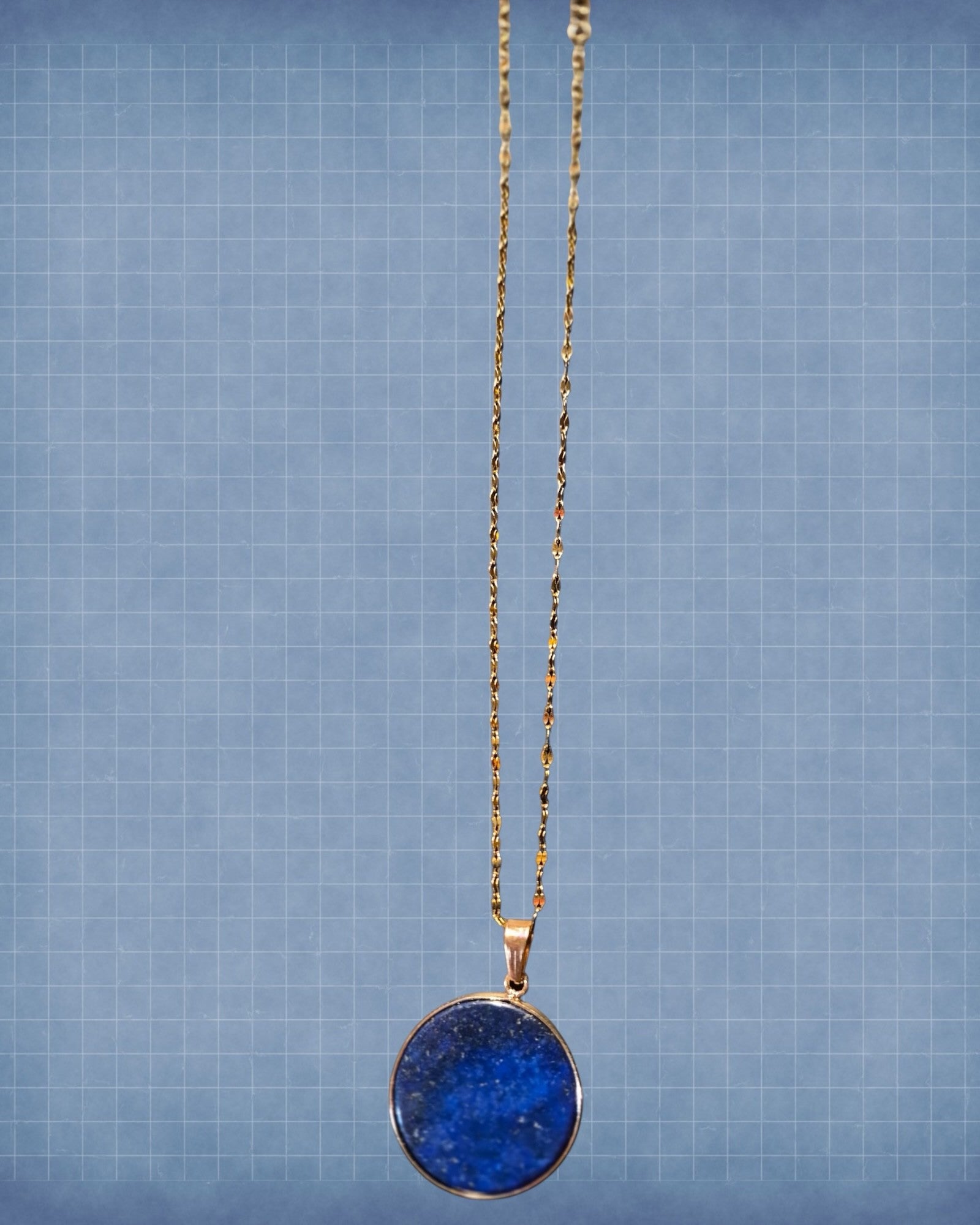 Heartfelt Creations round lapis lazuli pendant necklace with a gold-tone textured chain on a blue grid background