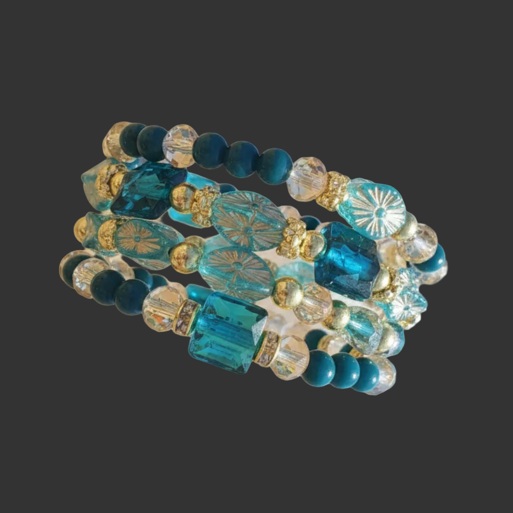 A close-up of a beaded bracelet with blue faceted beads, dark blue round beads, clear crystal beads, and gold-toned spacer details, shown against a softly blurred beige and white background.