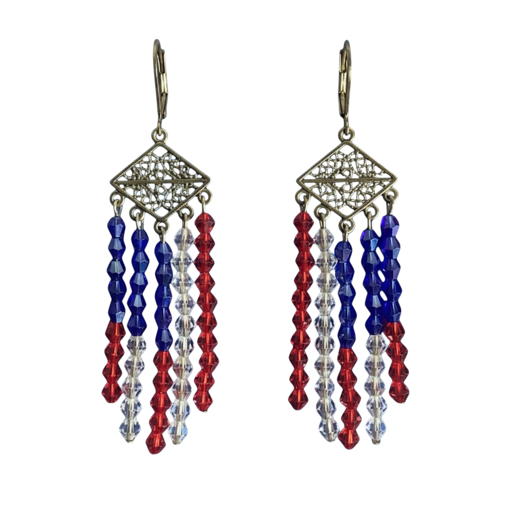 A pair of dangling earrings with ornate gold-tone filigree diamond-shaped tops and three hanging strands of faceted beads in royal blue, red, and clear, shown against a dark blue starry sky background.