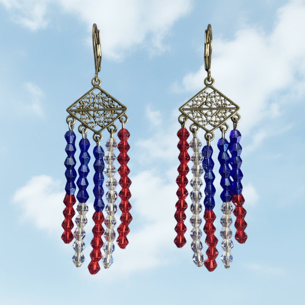 A pair of dangling earrings with ornate gold-tone filigree diamond-shaped tops and three hanging strands of faceted beads in royal blue, red, and clear, shown against a dark blue starry sky background.