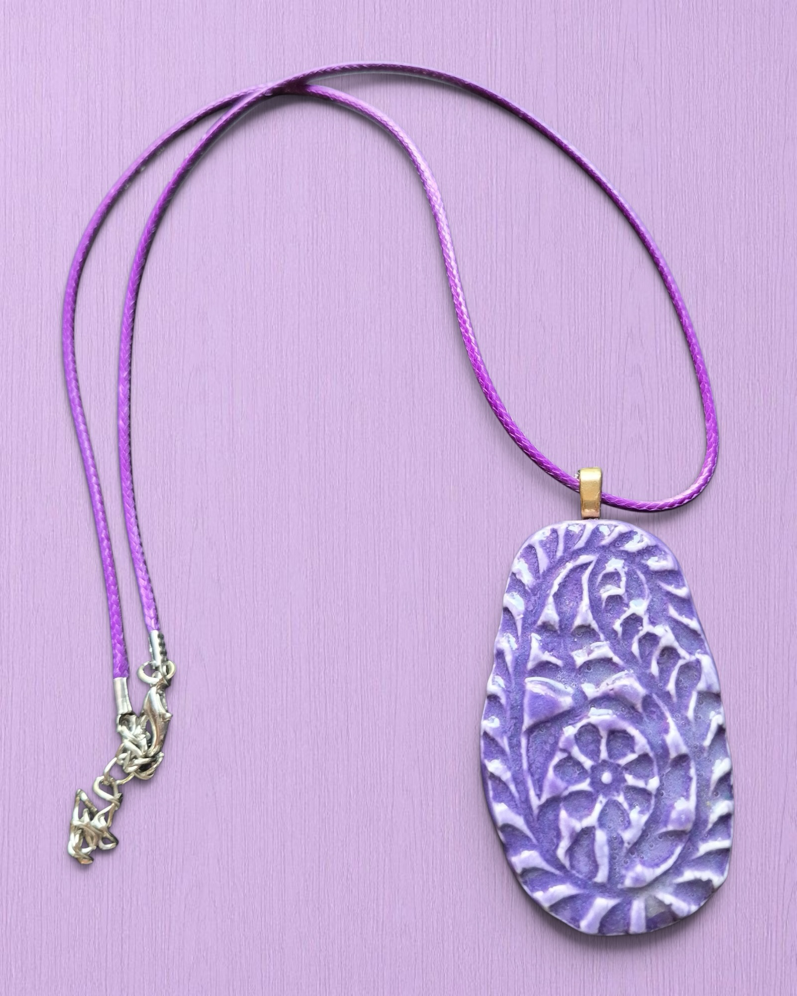 Heartfelt Creations purple ceramic pendant necklace with hand-carved floral texture on a matching cord.