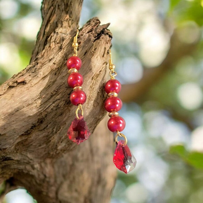 Heartfelt Creations crimson pearl and red crystal drop earrings with gold-tone accents hanging on a textured tree branch