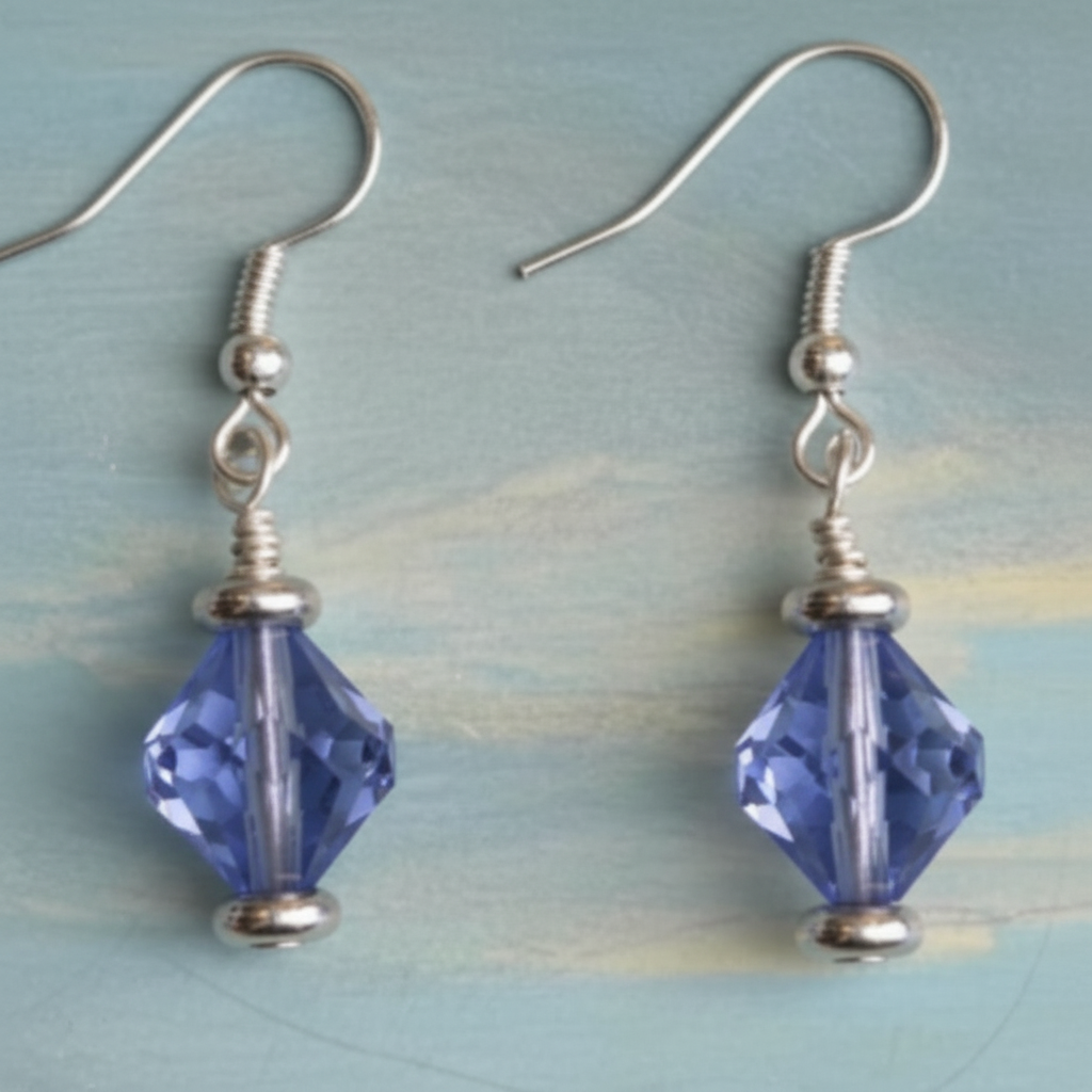A pair of silver-toned dangle earrings with faceted dark blue beads, displayed on a textured light blue and yellow painted background.