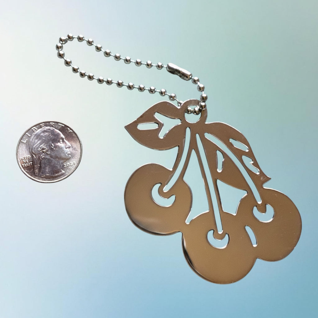 Heartfelt Creations silver-plated brass  metal cherry keychain with a ball-chain attachment shown next to a US quarter coin.
